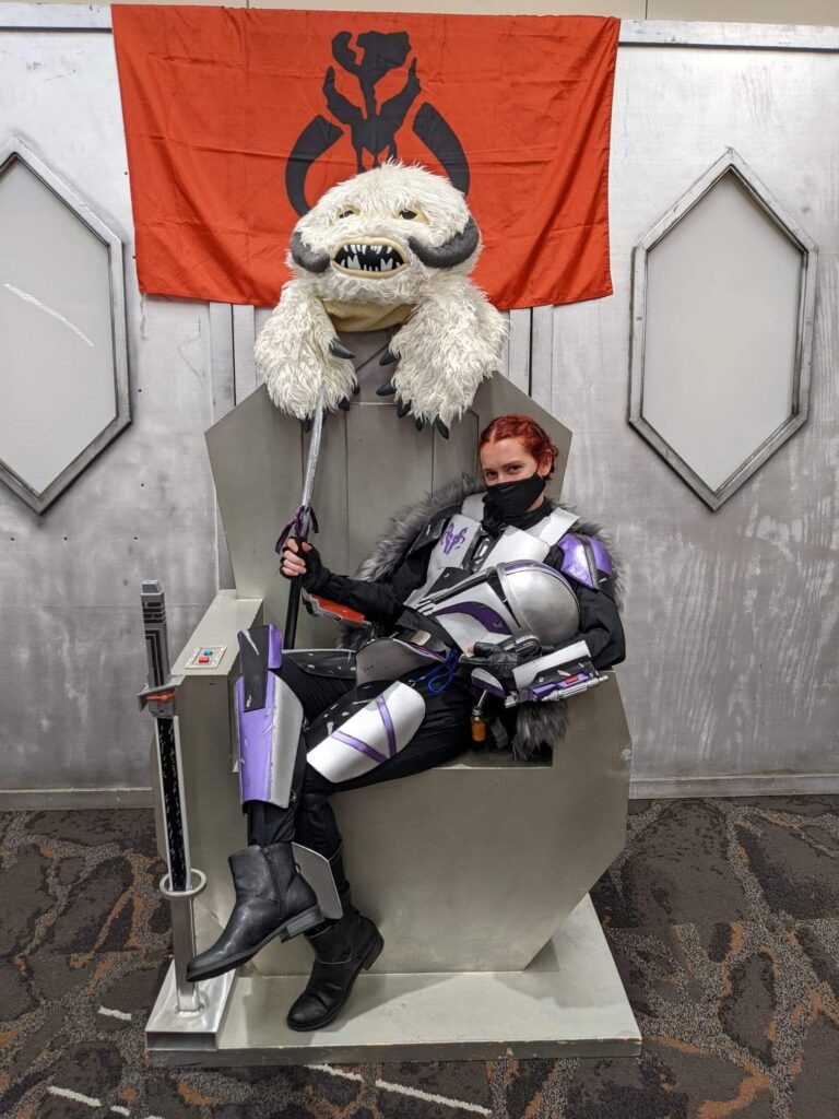 Me, dressed as my original character Mandalorian, sitting on a throne.