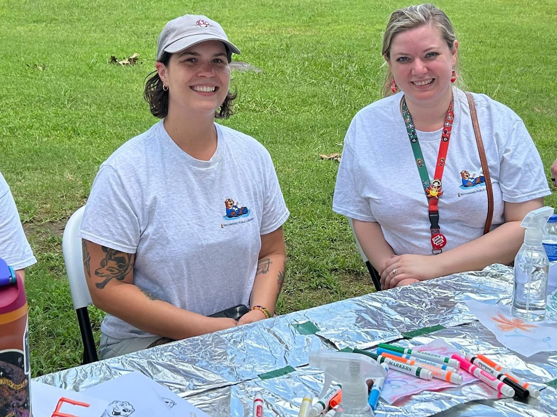 Richmond Public Libraries' Youth Services Team sits smiling at a table covered in aluminum foil. Markers, water bottles, and doodles are on top of the table.