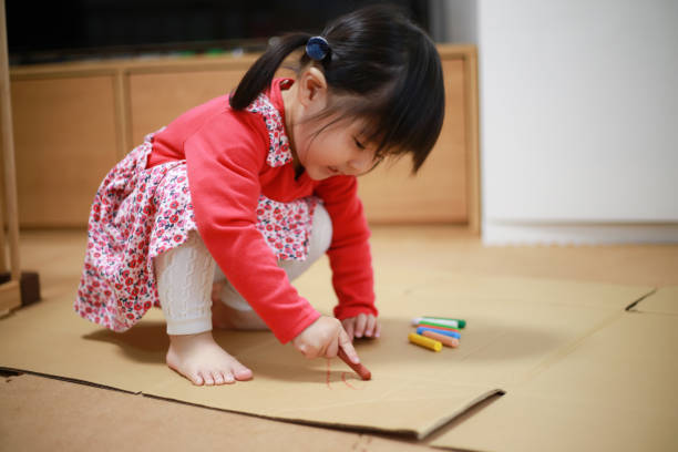 Toddler drawing with crayons on cardboard that is on the floor.