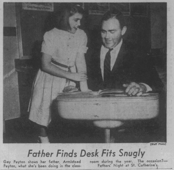 Image of Newspaper clipping of a standing child gazing at her father who sits uncomfortably in her school desk. Caption reads: "Father Finds Desk Fits Snugly. Gay Peyton shows her father, Armistead Peyton, what she's been doing in the classroom during the year. The occasion?- Fathers' Night at St. Catherine's. [staff photo]