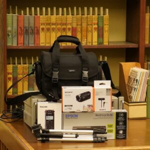 Image of RPL's Personal Archiving Kit. Features a camera bag, audio recorder, camcorder, lavalier microphone, tripod, and portable scanner. All materials sit on wooden table.