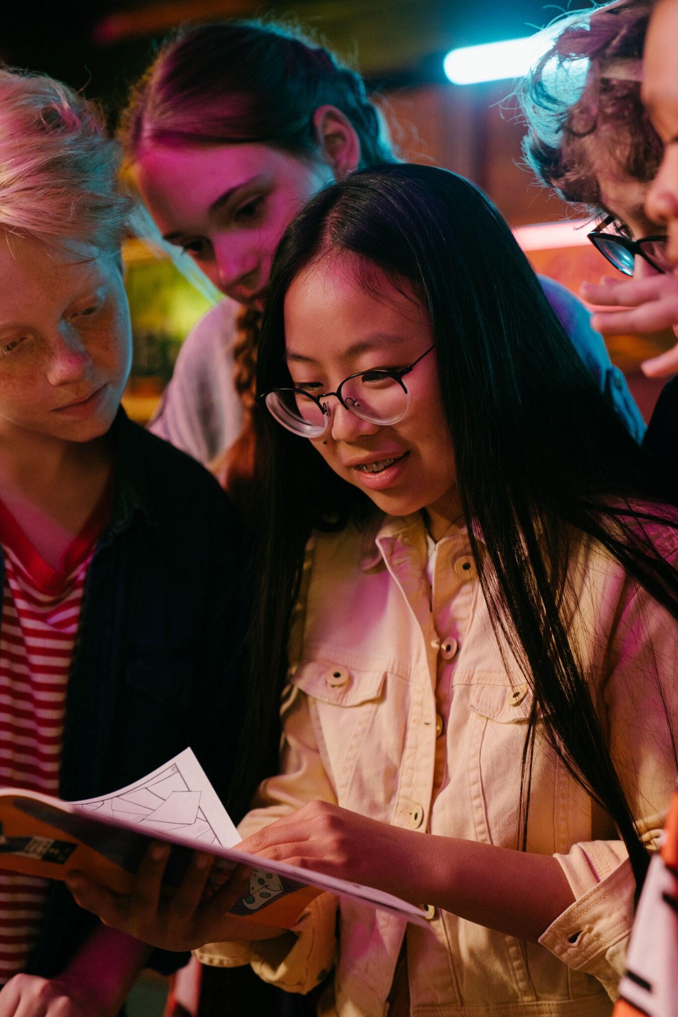 A group of five young adults huddle together to read an open graphic novel.