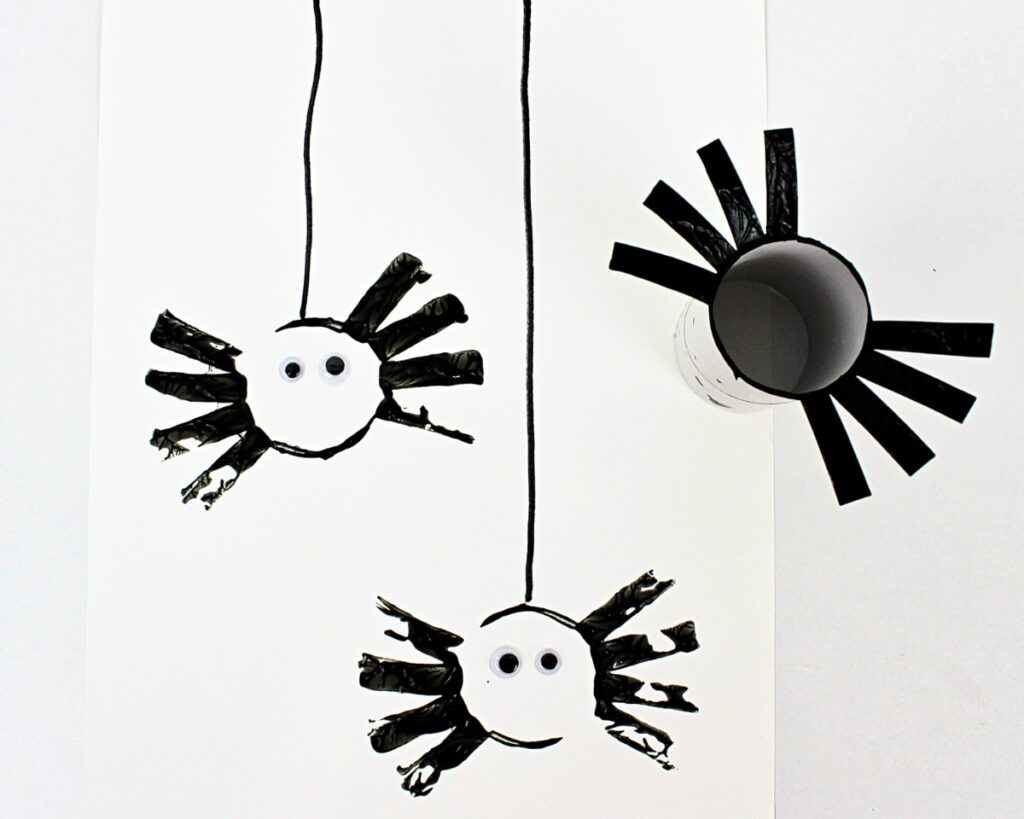 An image of black painted, paper-roll spider stamps on a white sheet of paper.